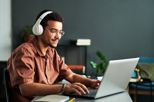 Male student at a laptop with headphones during a tutoring session and smiling